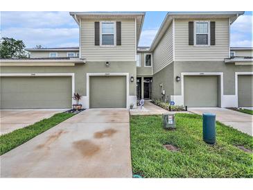 View of townhomes with light exteriors and single-car garages, accented with landscaping at 2844 Jacob Crossing Ln, Holiday, FL 34691