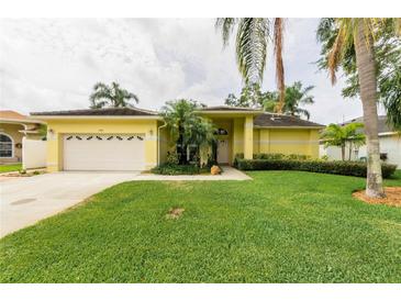 Charming yellow home with a well-manicured lawn and lush tropical landscaping, including mature palm trees at 1051 Glynwood Pl, Dunedin, FL 34698