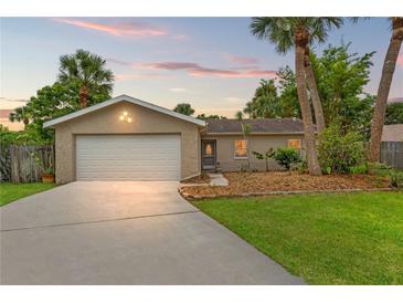 Charming single-story home featuring an attached garage, well-maintained lawn, and mature palm trees against a beautiful sunset sky at 1909 Dover Ct, Oldsmar, FL 34677