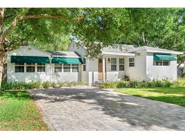 Charming white home with green awnings and a beautiful brick driveway framed by mature trees and lush landscaping at 4616 S Matanzas Ave, Tampa, FL 33611