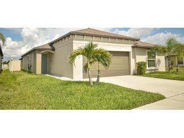 Beige single-story home featuring a two-car garage, palm trees, and a well-manicured lawn at 16623 Carlton Pond St, Wimauma, FL 33598