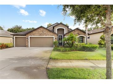 Charming single-Gathering home featuring a stone facade, three-car garage, and lush landscaping at 12729 Flatwood Creek Dr, Gibsonton, FL 33534