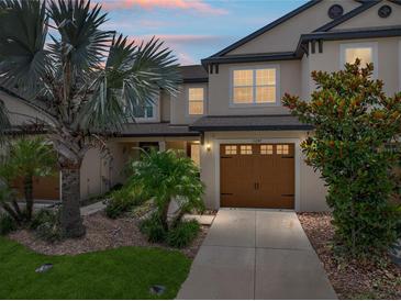 Charming townhome showcasing a well-manicured lawn, a brown garage door and mature trees and landscaping at 11287 Cay Spruce Way, San Antonio, FL 33576