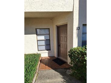 Inviting condo front door with tan exterior, decorative landscaping, and visible unit number at 3536 Countrybrook Ln # 13, Palm Harbor, FL 34684