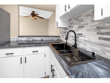 Kitchen with stainless sink, gray backsplash, granite counters, and white cabinetry at 1881 Lichen Ln # B, Clearwater, FL 33760