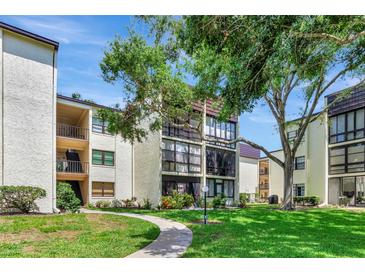Beautiful condo building with manicured lawn and mature trees against a sunny sky at 14130 Rosemary Ln # 3202, Largo, FL 33774