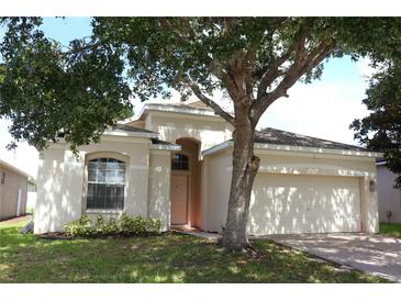 Beige single-story home featuring mature landscaping, arched entry, and a two-car garage at 221 Fairmont Dr, Spring Hill, FL 34609