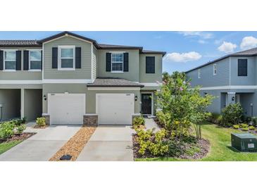 Charming townhome featuring a two-car garage, manicured lawn, and lush landscaping at 36414 Well Hill Way, Zephyrhills, FL 33541