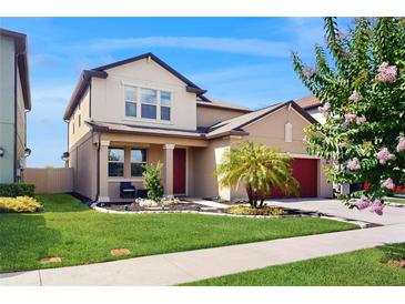 Charming two-story home featuring a manicured lawn, red garage door, and a welcoming front porch with white columns at 8747 Flourish Dr, Land O Lakes, FL 34637
