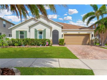 Charming single-story home with a well-manicured lawn, lush landscaping, and a brick driveway leading to a two-car garage at 11423 Brighton Knoll Loop, Riverview, FL 33579