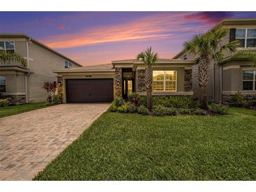 Charming single-Gathering home featuring lush landscaping, a stone facade, and a paver driveway under a beautiful sky at 3318 Woodland Brook Way, Wesley Chapel, FL 33543