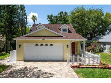 Charming, light yellow home featuring a brick paved driveway, a manicured lawn, and a white picket fence at 346 Gray Oak Dr, Tarpon Springs, FL 34689