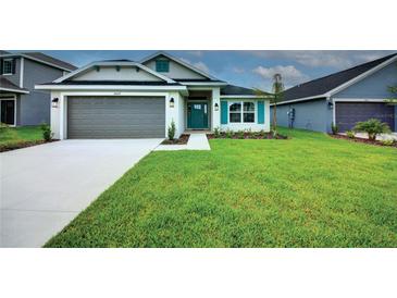 Charming single-story home with a well-manicured lawn, gray garage door, and teal-colored front door at 16425 66Th E Ln, Parrish, FL 34219