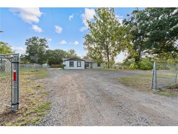 Wide shot of a white, one-story home with a gravel driveway and fenced yard at 221 S Kingsway Rd, Seffner, FL 33584