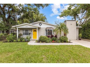 Charming single-story home with a bright yellow door and well-manicured landscaping at 1226 E Henry Ave, Tampa, FL 33604