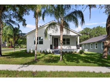 Charming white home with a manicured green lawn, palm trees and inviting front porch with black trim at 5709 N 20Th St, Tampa, FL 33610