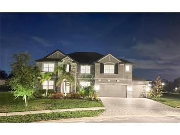 Night view of a two-story home featuring stone accents, a three-car garage, and manicured landscaping at 9508 Pyrenees Pl, Seffner, FL 33584