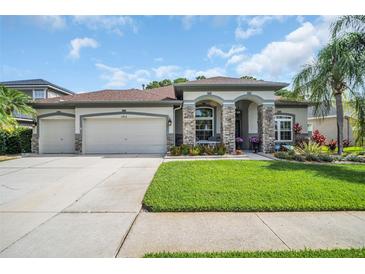 Charming home with a three-car garage, stone accents, lush landscaping, and well-manicured lawn at 12918 Tar Flower Dr., Tampa, FL 33626