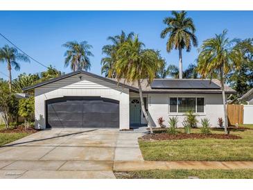 Charming single-story home showcasing a brick facade, dark garage door, and lush landscaping with mature palm trees at 6000 Denver Ne St, St Petersburg, FL 33703