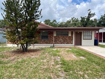 Single-story brick house featuring a welcoming front porch and a mature tree in the yard at 9218 N 52Nd St, Tampa, FL 33617