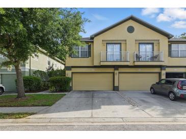 Two-story tan townhome featuring dual car garages, a small balcony, and verdant landscaping at 27563 Pleasure Ride Loop, Wesley Chapel, FL 33544
