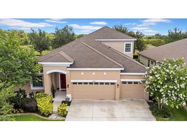 Two-story tan home with three car garage, red front door, and well maintained landscaping at 32624 Summerglade Dr, Wesley Chapel, FL 33545