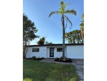 Single-story home with white exterior, black trim, landscaping and brick walkway, set against a blue sky at 7703 Glenview Ln, Tampa, FL 33615
