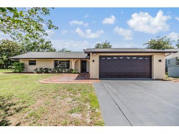 Charming single-story home with a well-manicured lawn, mature trees, and a two-car garage on a sunny day at 4228 Belle Isle Ct, New Port Richey, FL 34653
