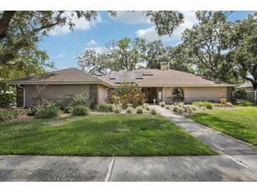 Charming single-story home with a well-manicured lawn, mature trees, and solar panels on the roof at 10902 Bent Tree Pl, Tampa, FL 33618