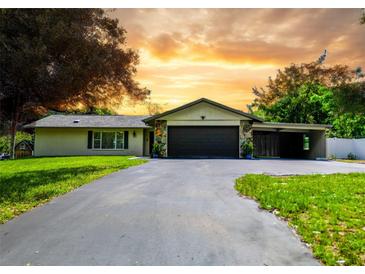 Charming single-story home with a welcoming driveway, lush lawn, and well-manicured landscaping under a beautiful sunset at 7211 Red Oak Loop, New Port Richey, FL 34654
