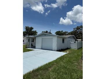 Single-story home with a white brick facade, attached garage, and a blue driveway at 5025 Tammy Ln, Holiday, FL 34690