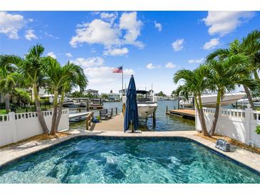 Beautiful pool view of boat dock with palms, boats, and a sunny sky at this lovely waterfront property at 16106 6Th E St, Redington Beach, FL 33708