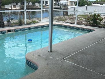 A refreshing, screened-in backyard pool with cool, clear water surrounded by a concrete deck near a waterfront canal at 13605 Stacey Dr, Hudson, FL 34667