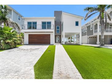 Modern two-story home with a wood garage door, landscaped yard and light brick driveway at 905 Bay Point Dr, Madeira Beach, FL 33708
