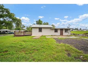 View of home from backyard, featuring a wood deck, green lawn, and cloudy blue skies at 37732 Cecil Ln, Zephyrhills, FL 33542
