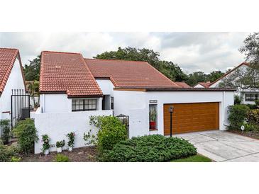 Charming home with a terracotta roof, white stucco walls, and a well-maintained front yard and a wood paneled garage door at 11501 Cerca Del Rio Pl, Temple Terrace, FL 33617