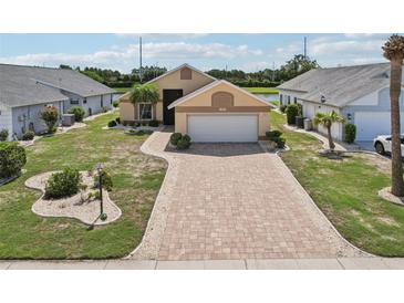 Charming single-story home featuring a brick paver driveway and well-manicured lawn, surrounded by lush landscaping at 1901 E Del Webb Blvd, Sun City Center, FL 33573