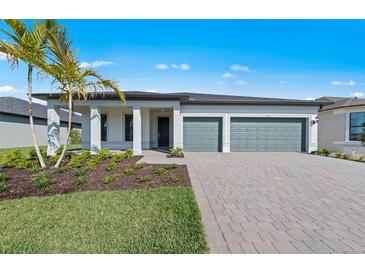 Beautiful single-story home featuring a manicured lawn, grey two car garage, and elegant white column entry at 2589 Winding Creek Trl, North Port, FL 34289