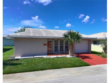 Charming single-story home featuring a well-manicured lawn, red driveway, and a decorative palm tree at 5390 Magnolia N Trl, Pinellas Park, FL 33782