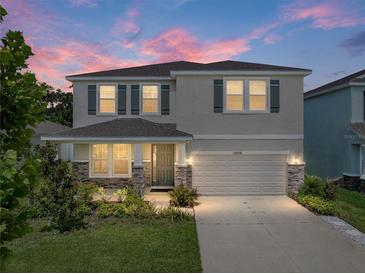 Charming two-story home featuring a well-manicured lawn, stone accents, gray exterior, and an attached two-car garage at 13735 Wineberry Dr, Dade City, FL 33525