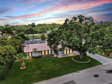 Beautiful home exterior features a large front yard, mature trees, and a screened-in pool at 2401 Roberta Ln, Clearwater, FL 33764
