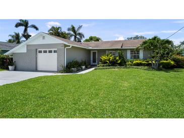 Charming single-story home with a well-manicured lawn and tropical landscaping, and a gray brick facade at 8718 Tahiti Ln, Tampa, FL 33615
