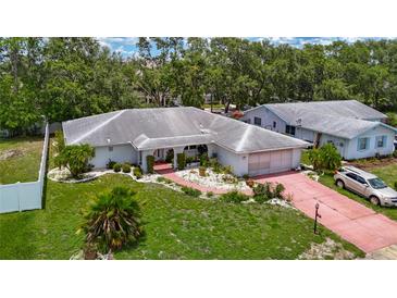 Inviting single-Gathering home featuring lush landscaping, a red brick driveway, and mature trees surrounding the property at 1607 New Bedford Dr, Sun City Center, FL 33573