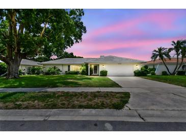 Charming single-story home featuring a well-manicured lawn, mature trees, and a two-car garage under a pastel sky at 2418 Cardwell Way, Sarasota, FL 34231