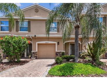 Charming townhome with a one-car garage, brick driveway, and lush landscaping at 26835 Juniper Bay Dr, Wesley Chapel, FL 33544