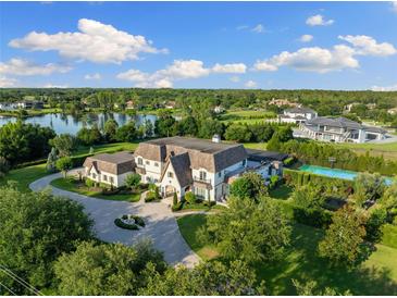 Expansive aerial view of an estate home with lush landscaping, a lake, and a tennis court under a bright blue sky at 18521 Wayne Rd, Odessa, FL 33556