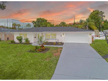 Charming home featuring a manicured front lawn, landscaping, and two-car garage against a beautiful sunset backdrop at 1723 Cypress Ave, Belleair, FL 33756