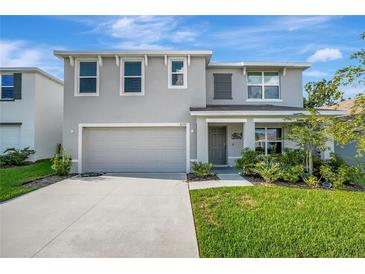 Two-story home showcasing a manicured lawn, neutral stucco, attached garage, and an inviting covered entryway at 7737 Rosewood Garden Loop, Tampa, FL 33637