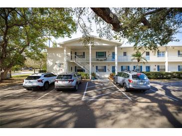 Condo building exterior with covered stairwells and mature trees creating shade for the parked cars at 500 Glennes Ln # 202, Dunedin, FL 34698