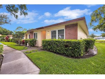 Charming single-story home with manicured lawn, lush greenery, and brick accents at 900 Maclaren N Dr # D, Palm Harbor, FL 34684